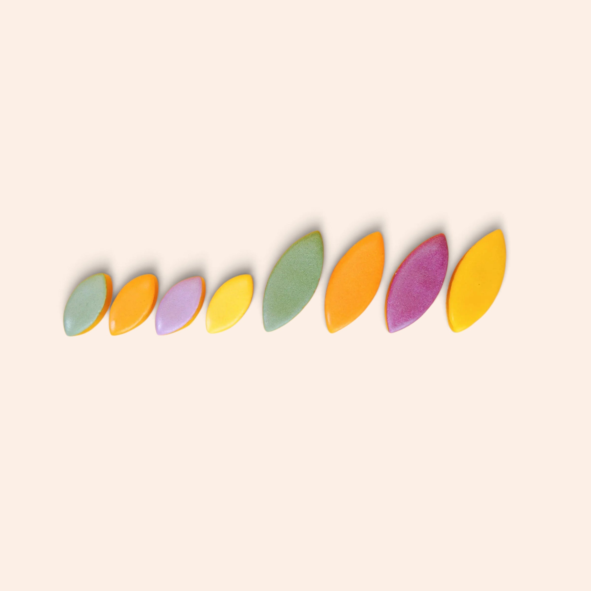 Assortiment de calissons fruités Maison Fruidoraix aux couleurs vives, disposés en ligne sur fond crème.