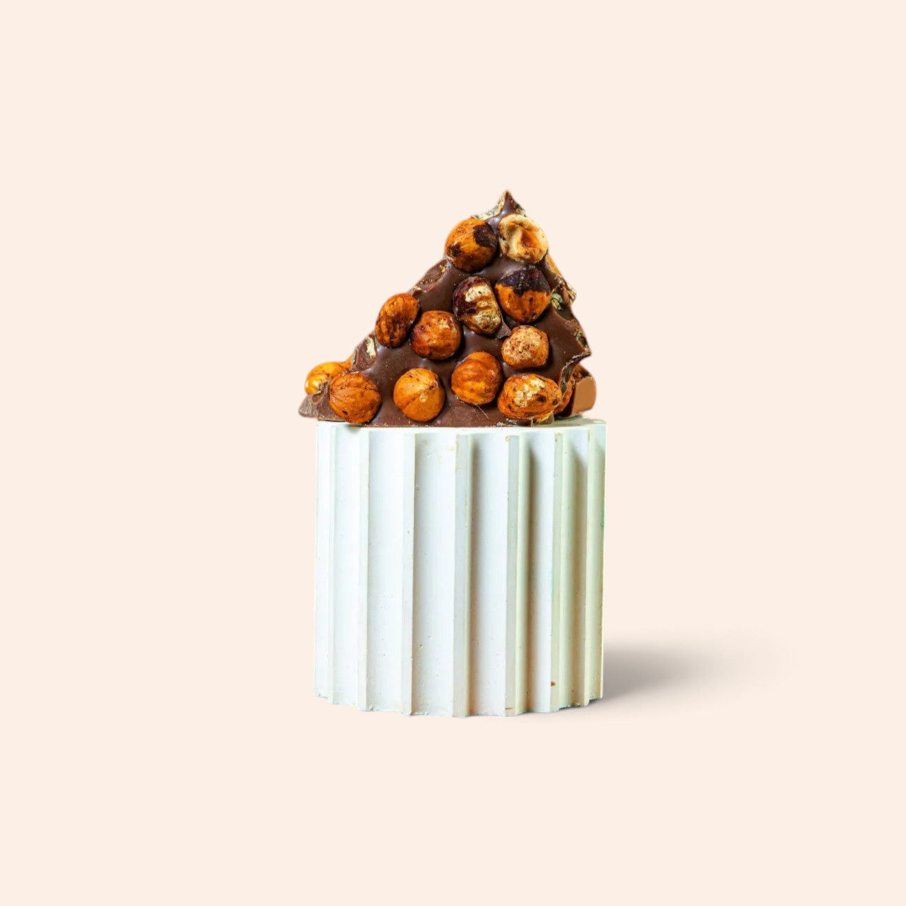 Morceau de chocolat au lait Maison Fruidoraix garni de noisettes entières torréfiées sur un socle blanc cannelé
