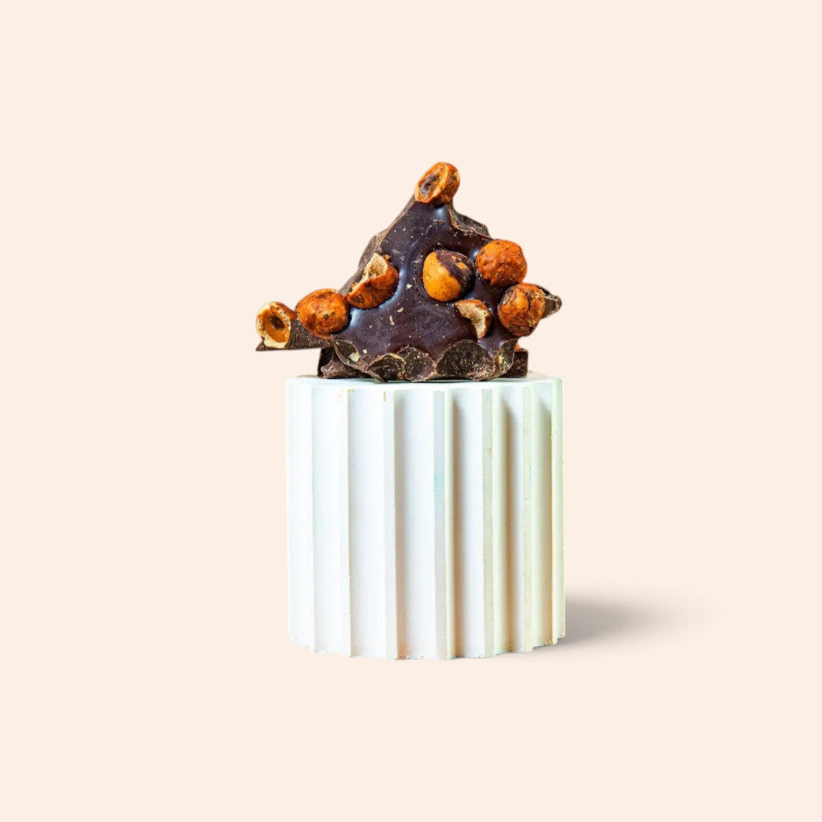 Morceaux de chocolat noir 74% cacao aux noisettes torréfiées Maison Fruidoraix sur un socle cannelé blanc