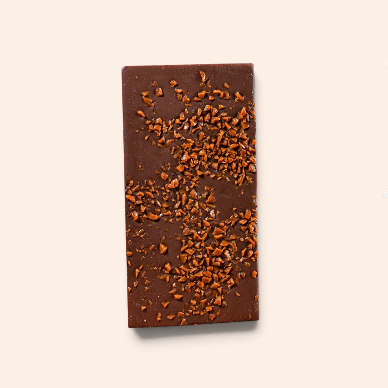 Tablette de chocolat au lait Maison Fruidoraix parsemée d'éclats de caramel croquant sur fond beige